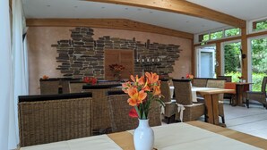 Un restaurante con mobiliario de mimbre, una pared de piedra y un jarrón blanco con flores.