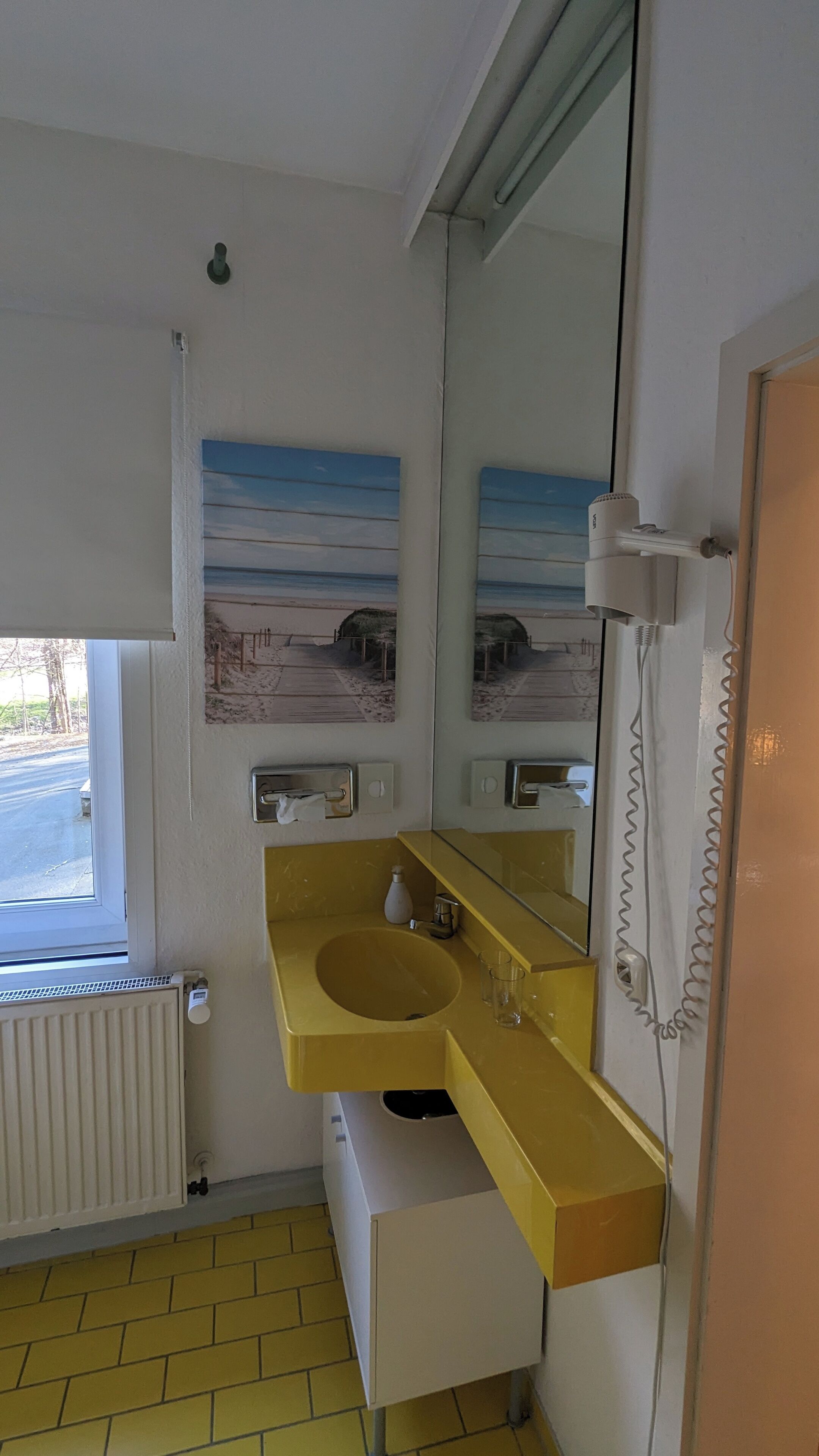 A bathroom with a yellow sink, a mirror, a towel rack, and a window with a view of a beach.
