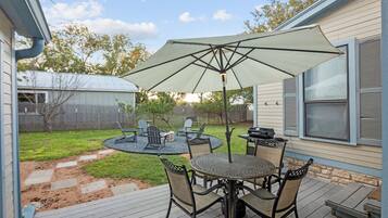 An outdoor patio with a table and chairs, a grill, and a large umbrella.
