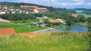 Ländliche Gegend mit einem großen Gebäude mit rotem Dach, umgeben von grünen Feldern und einem Gewässer.