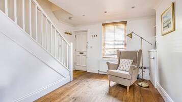 A hallway with wooden flooring, a staircase, a white door, and a window with blinds.