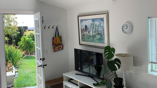 Ett modernt vardagsrum med en takfläkt, en platt-TV, en växt och ett fönster med persienner.
