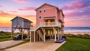 Une maison à deux étages située en bord de mer, dotée d’un balcon, d’une terrasse couverte et d’une structure typique des maisons de plage.
