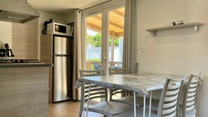 Eine kompakte Küche mit Edelstahl-Kühlschrank, Mikrowelle und Gasherd. Ein Essbereich mit Tisch und Stühlen sowie ein Fenster mit Vorhängen.