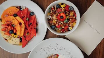 Three bowls of fruit and granola on a wooden table with a menu.