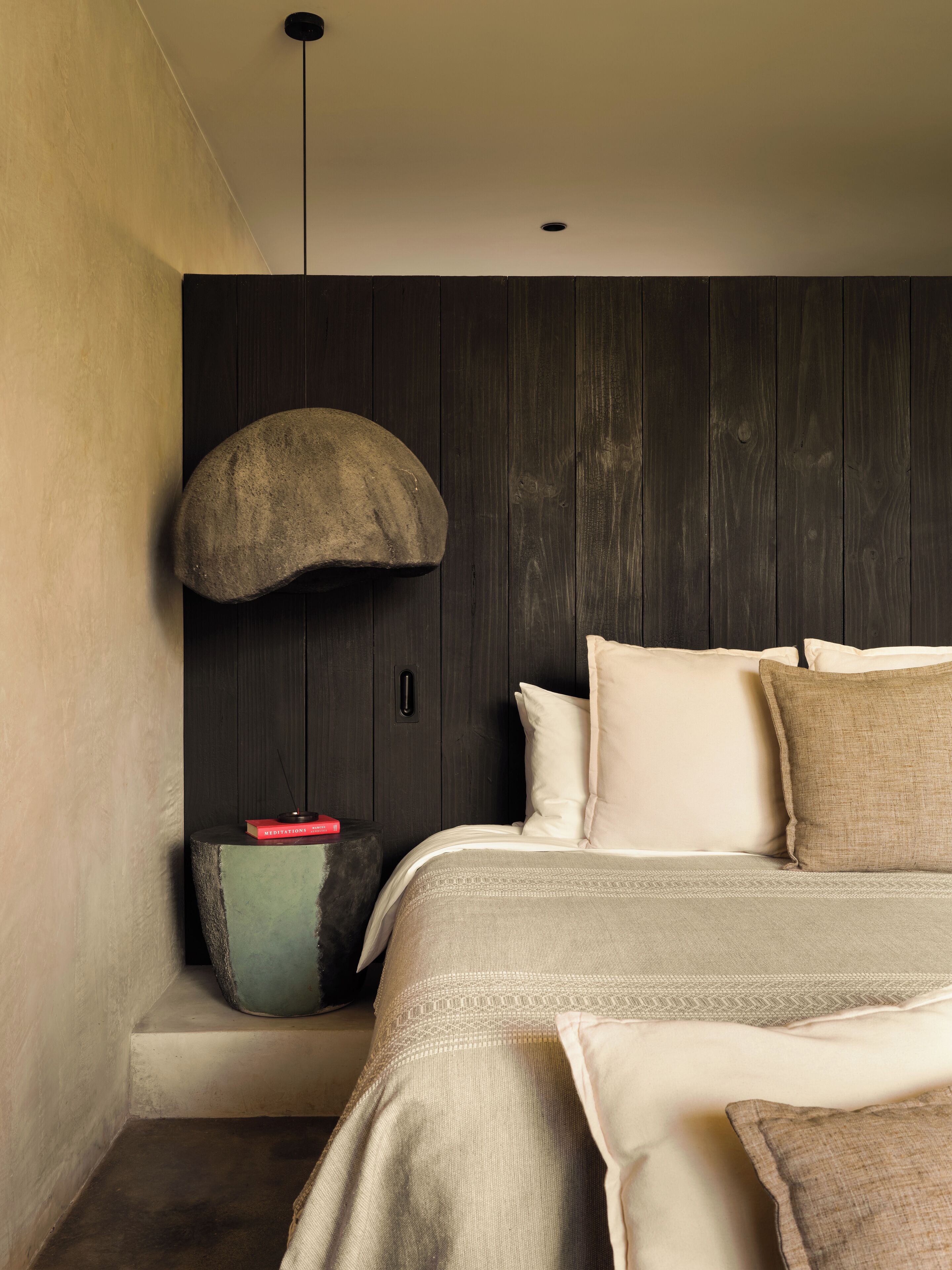 Un dormitorio moderno con cama, almohadas, una mesita auxiliar pequeña y una lámpara de pared de diseño único.