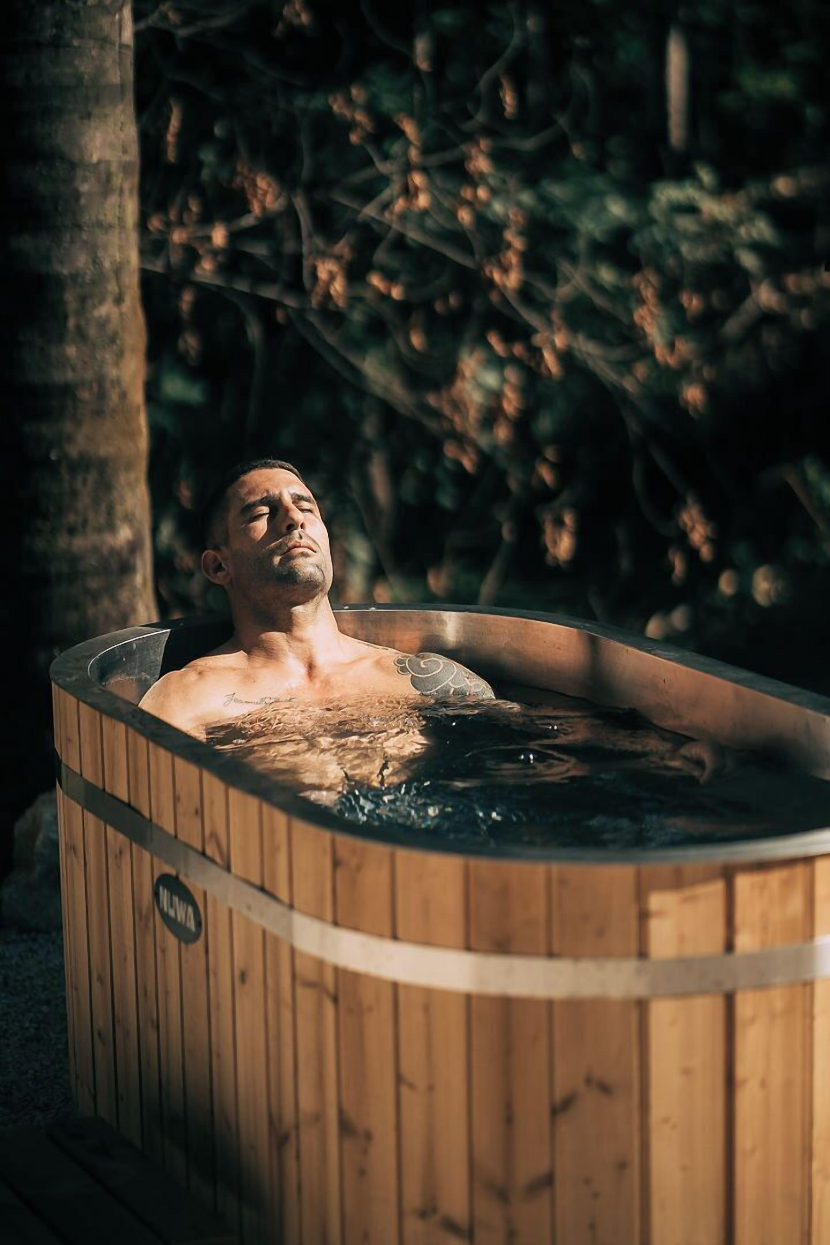 A wooden hot tub with a person inside, surrounded by trees.