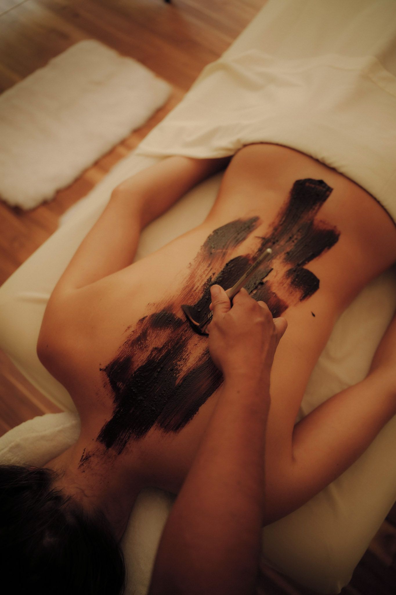 Une personne allongée sur une table de massage, avec des marques noires sur le dos, indiquant qu’elle a reçu un soin corporel.