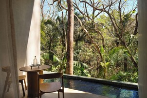 Zona junto a la piscina con mesa y sillas, rodeada de exuberante follaje y árboles.