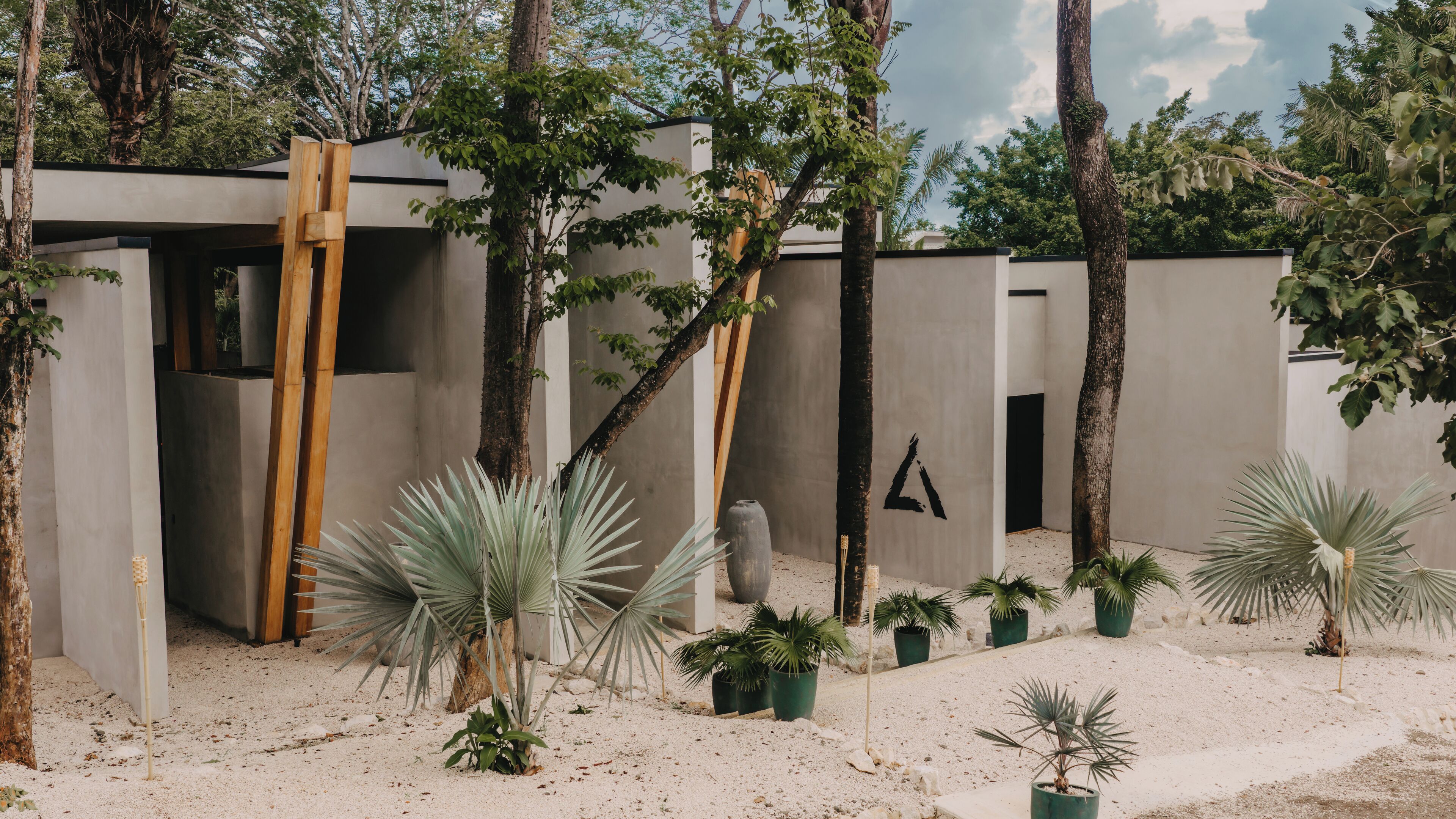 A modern outdoor area with a minimalist design, featuring a concrete wall, a wooden structure, and various potted plants.