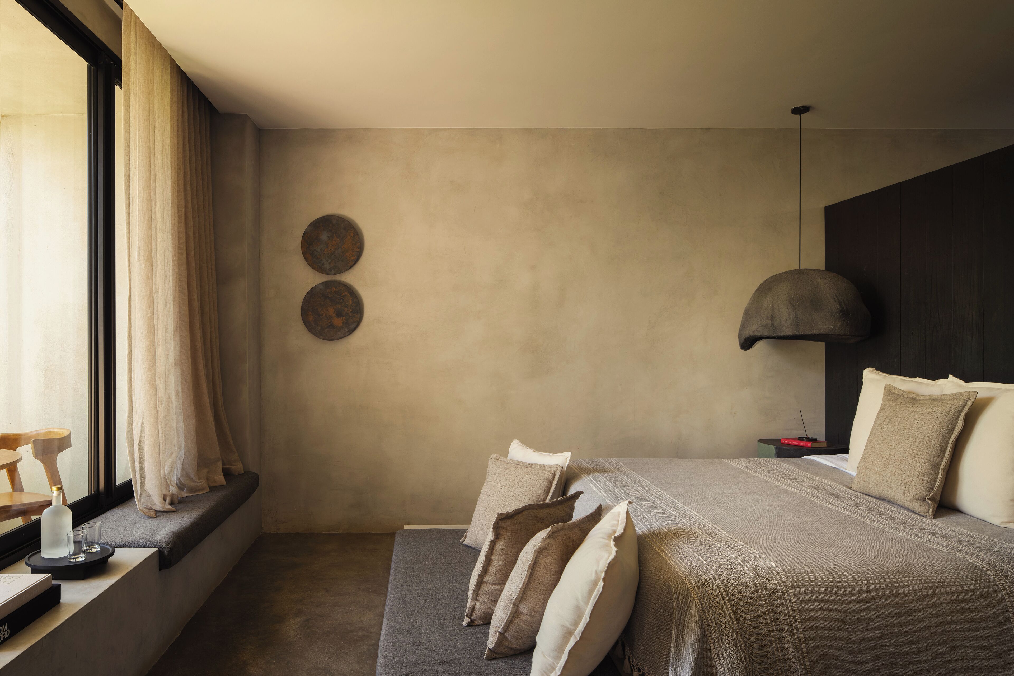 A modern bedroom with a large bed, a window with curtains, a bedside table, and a wall-mounted lamp.