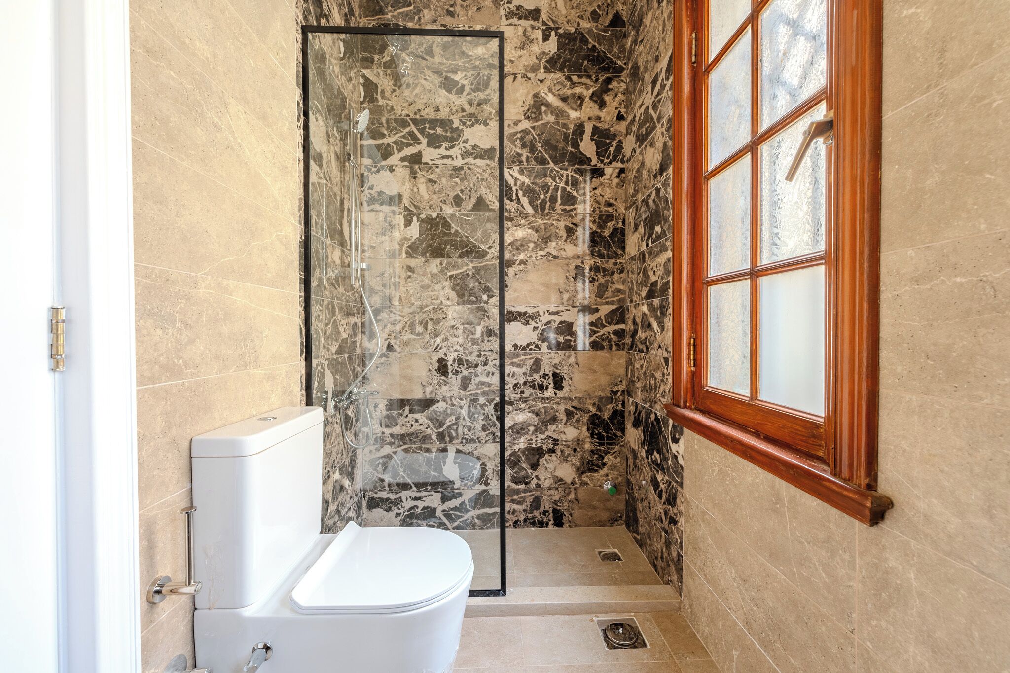 Un bagno con cabina doccia in marmo, un WC e una finestra con stipiti in legno.