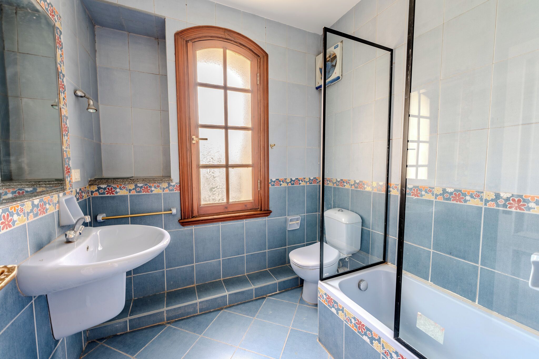 A bathroom with a sink, toilet, and bathtub, featuring blue tiles and a wooden-framed window.