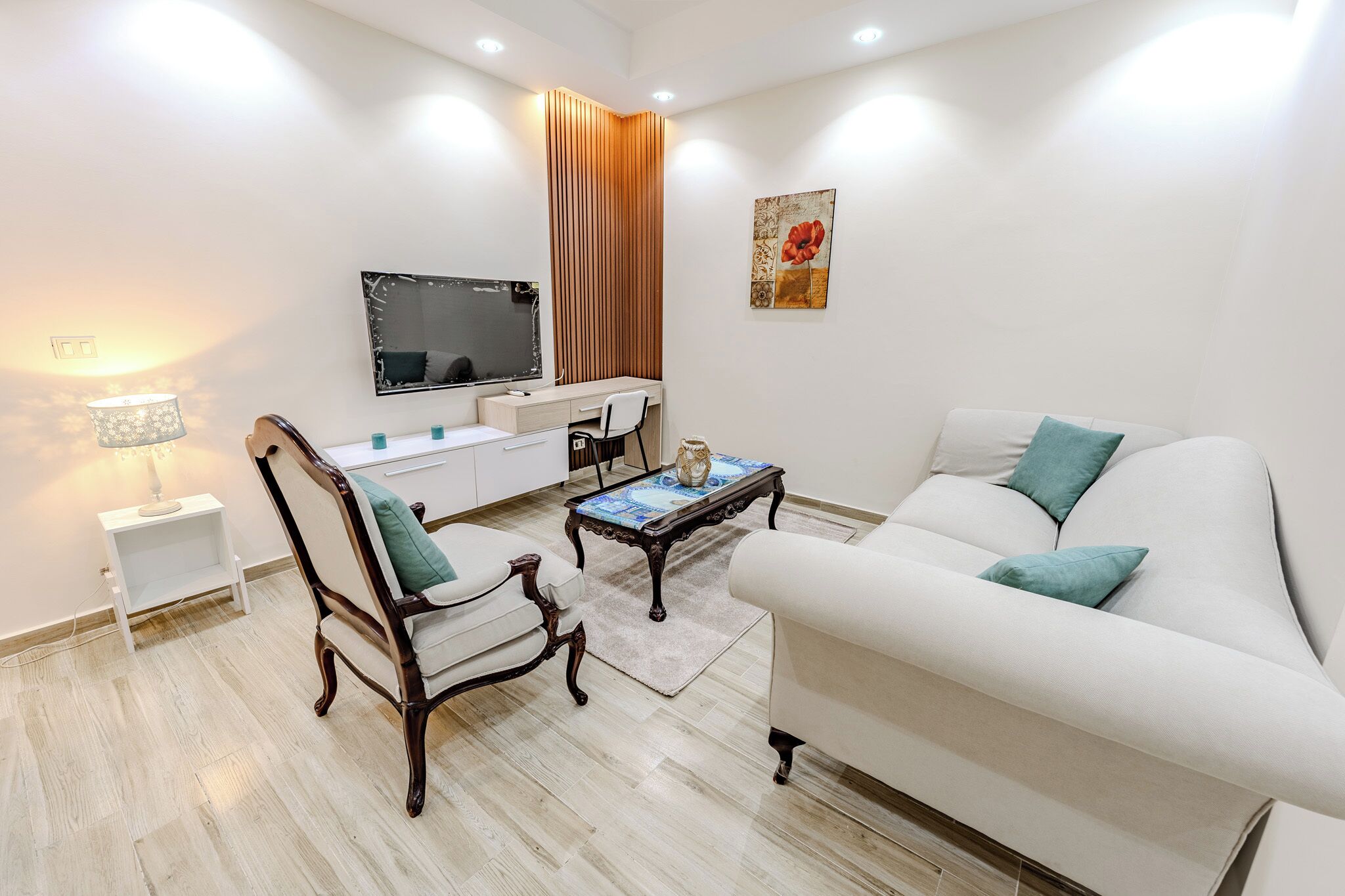 A modern living room with a white sofa, a wooden chair, a coffee table, a TV, and a desk.