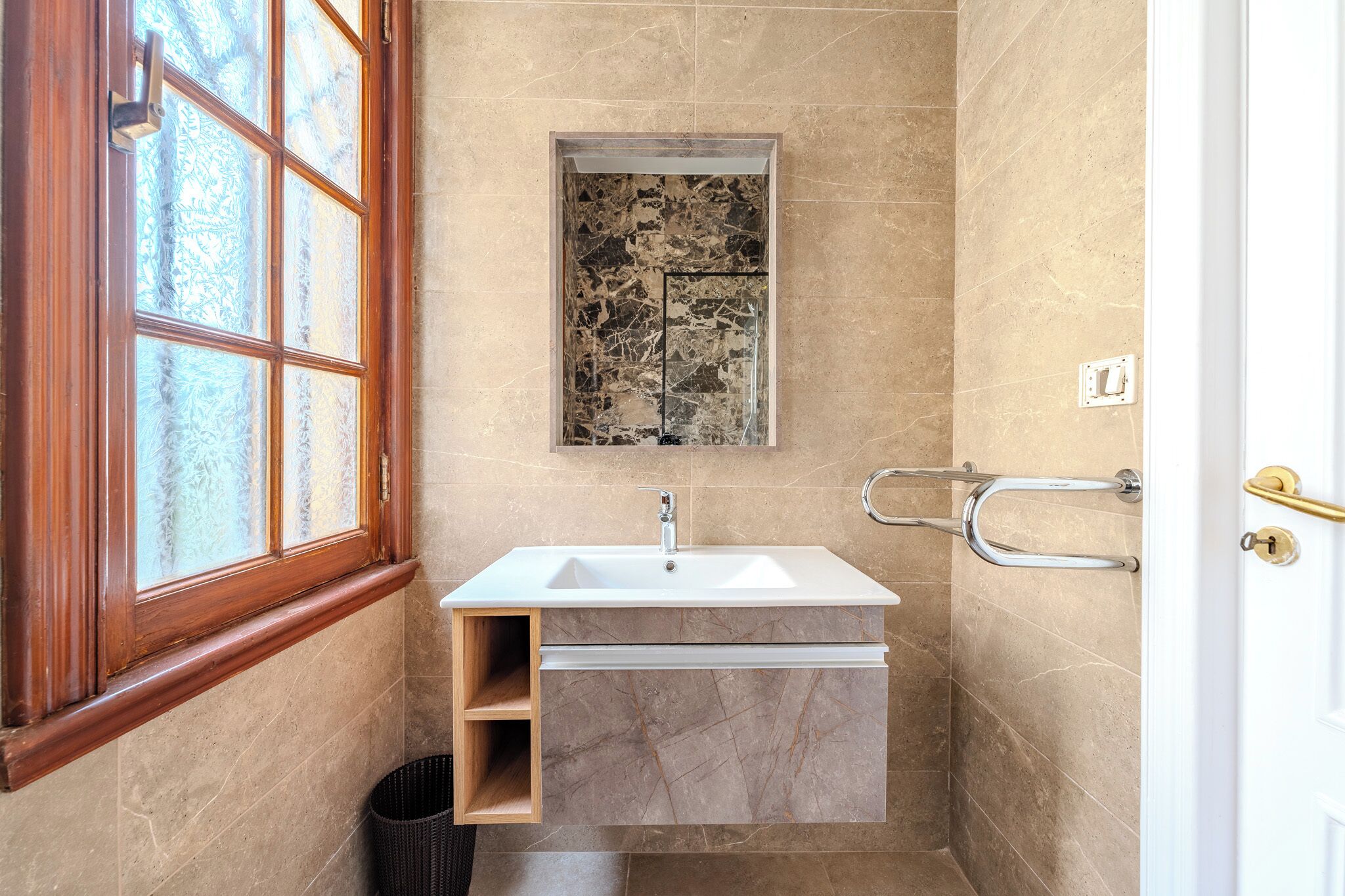 A bathroom with a marble sink, a window with frosted glass, and a towel rack.