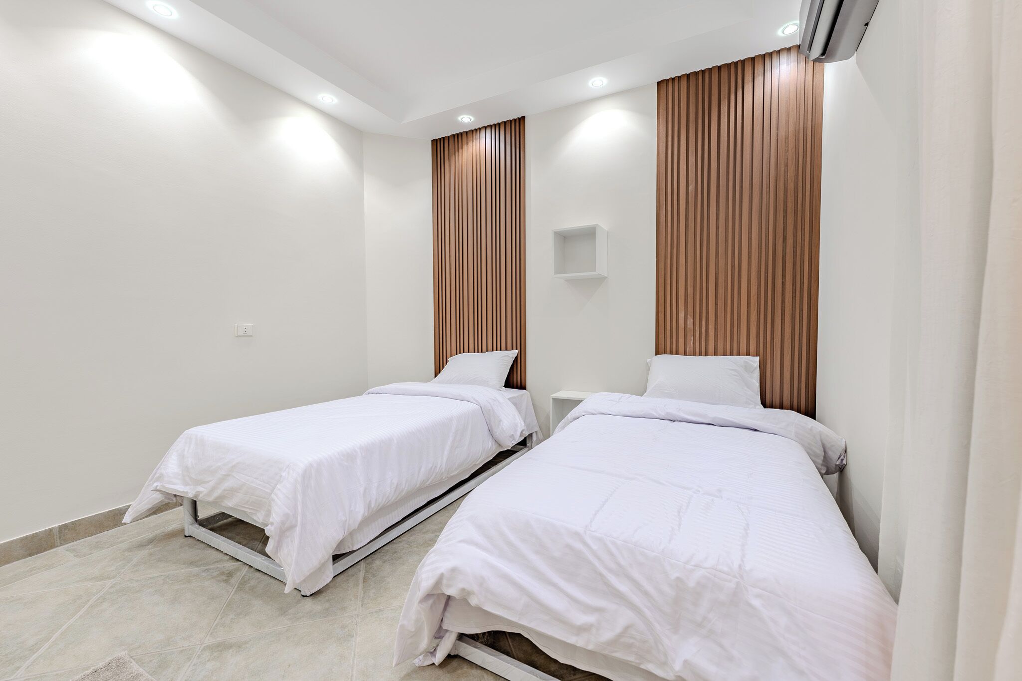 A hotel room with two single beds, a wooden panel wall, and recessed ceiling lights.