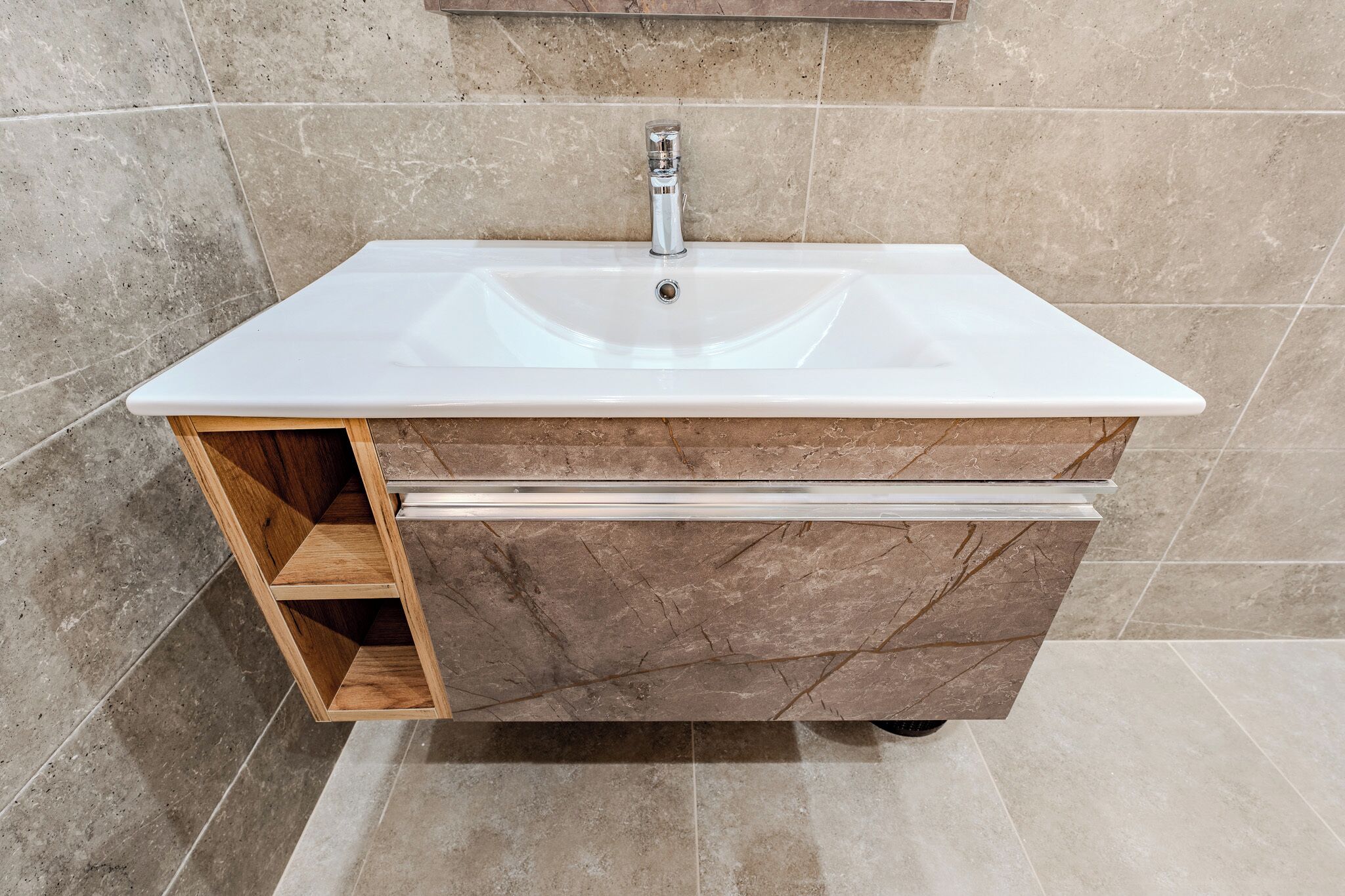 A bathroom with a white sink, wooden cabinet, and marble tiles.