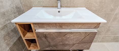 A bathroom with a white sink, wooden cabinet, and marble tiles.