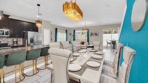 A modern kitchen with dark cabinets, a stainless steel refrigerator, and a bar area with green chairs. - Champions Gate Resort Townhome with Private Pool (Davenport)
