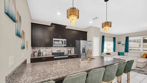 A modern kitchen with granite countertops, dark cabinets, stainless steel appliances, and a central island with bar stools. - Champions Gate Resort Townhome with Private Pool (Davenport)