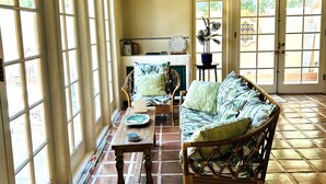 Una habitación amplia con ventanas grandes, piso de madera y una zona de estar con sofá y sillones.