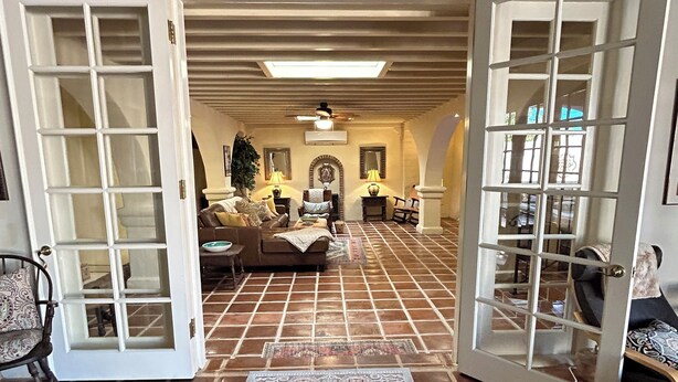 Un salón amplio con suelo de baldosas, un conjunto de sofás y una mesa de centro. Hay dos puertas abiertas que dan a otra habitación.