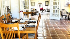 Un comedor con una mesa de madera dispuesta para cuatro personas, rodeada de sillas. Se observan dos puertas que dan a otra habitación, y un ventilador de techo.