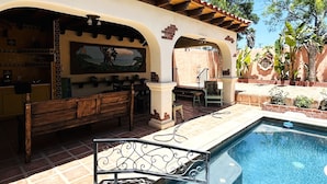 Un área de piscina con terraza de madera, mesa de billar y zona de estar cubierta.