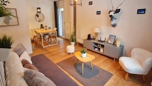 Un salon avec un canapé, une table basse ornée d’une plante, un meuble gris et une chaise blanche.