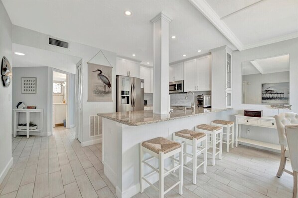 A modern kitchen with white cabinetry, a central island with bar stools, and a dining area with a white chair.