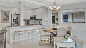 A modern kitchen with white cabinetry, a central island with stools, a dining table, and a chandelier. - Bay View CLOSE to Beach, Shops, Restaurants, Marina (Bradenton Beach)