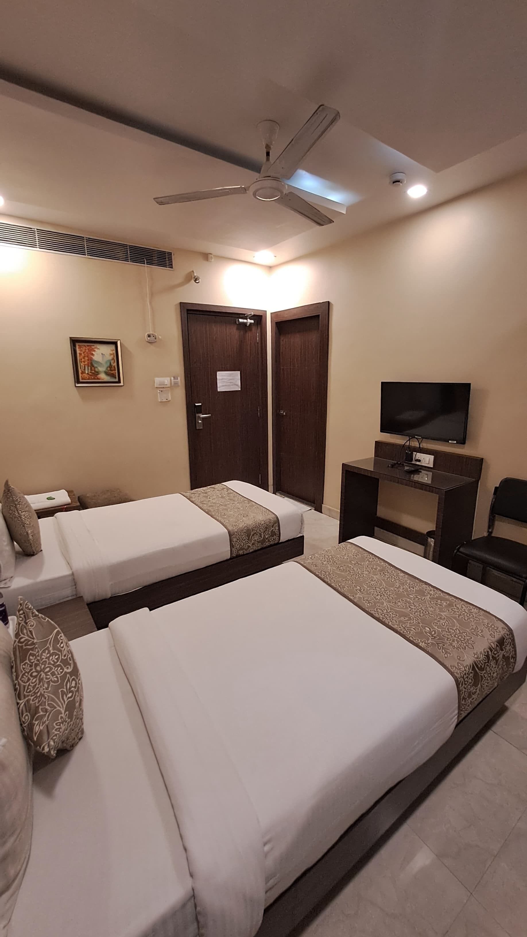 A hotel room with two single beds, a ceiling fan, a TV, and a desk.