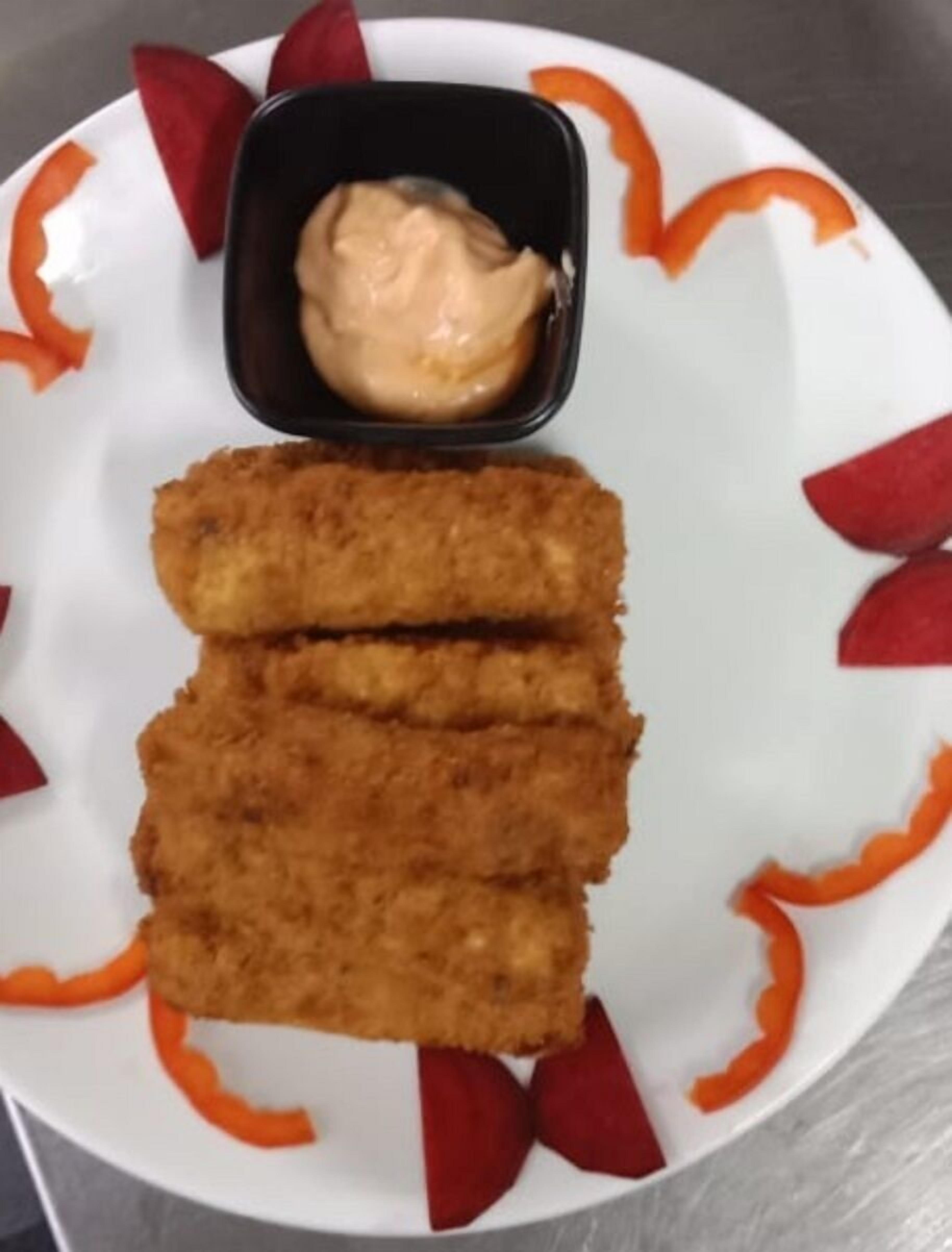 Un plato con dos porciones de comida rebozada y un recipiente pequeño de salsa, rodeado de rodajas de zanahoria.