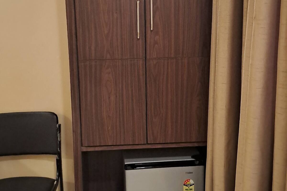 Quarto com guarda-roupa, uma cadeira e um pequeno frigorífico.