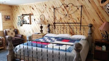 Une chambre avec un mur recouvert de lambris en bois, un lit avec une courtepointe, une table de chevet, une chaise et un ventilateur de plafond.
