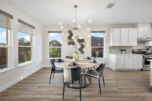 A modern kitchen with white cabinets, a central island, and a dining area with a round table and chairs.