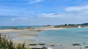 A coastal landscape with a sandy beach, clear blue water, and a distant rocky outcrop.