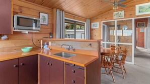 Una cocina compacta con armarios de madera, un microondas, un lavamanos y una zona de comedor con sillas de madera.
