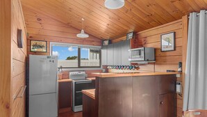 Una cocina compacta con paredes de madera, un refrigerador, una estufa, un microondas y una ventana con vista a una cerca.