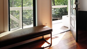 A room with a bench, large windows, and a view of a balcony with trees.