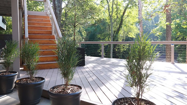A wooden deck with potted plants, a staircase, and a railing overlooking a forested area.