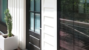 A white exterior with a black door and window, a small planter with a plant, and a black wall-mounted light fixture.