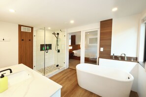 Un baño moderno con ducha envuelta en vidrio, una bañera independiente y un mueble de tocador de madera.