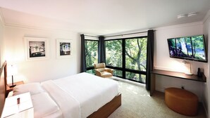 A modern hotel room with a large bed, a TV, a chair, and a desk.