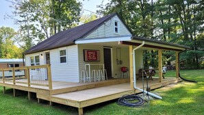 A small, single-story wooden house with a porch, a sign reading "Double Z+2 Cottage," and outdoor seating.