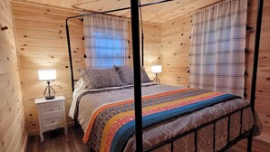 A wooden cabin bedroom with a four-poster bed, two bedside tables, and a window with curtains.
