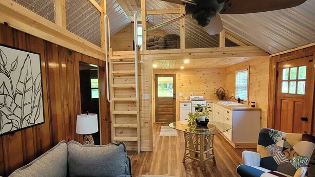 A cozy cabin interior with a loft bedroom, a dining area, and a kitchen.