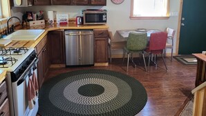 Una cucina con mobili in legno, un forno a microonde, un lavello e una stufa. Sul pavimento c'è un tappeto verde e una finestra con vista.