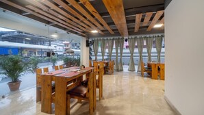 A dining area with wooden tables and chairs, a glass wall, and a view of the street outside. - Treebo Kashvijoy (Guwahati)