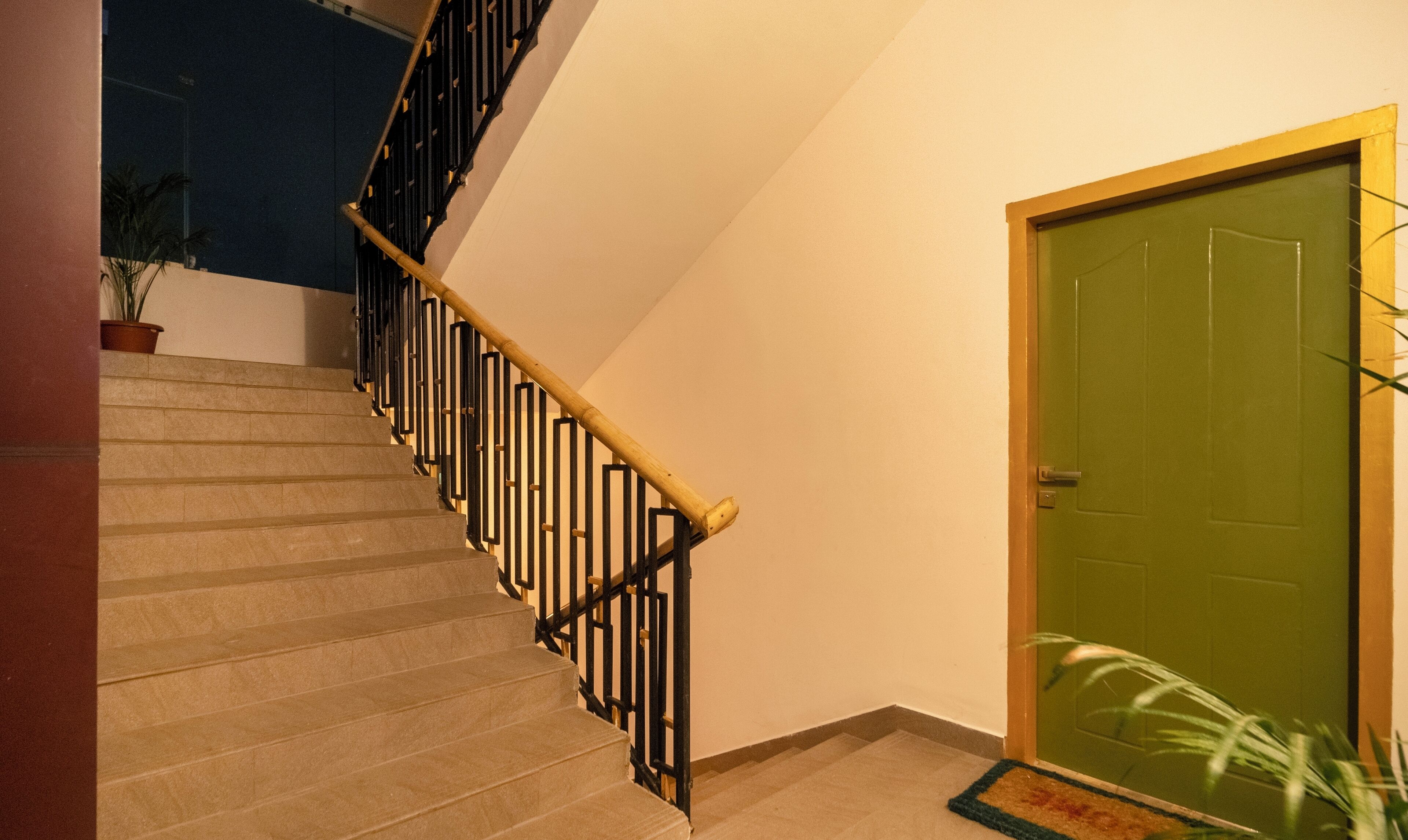 A staircase with a wooden handrail and black balusters, leading to a green door with a doormat.
